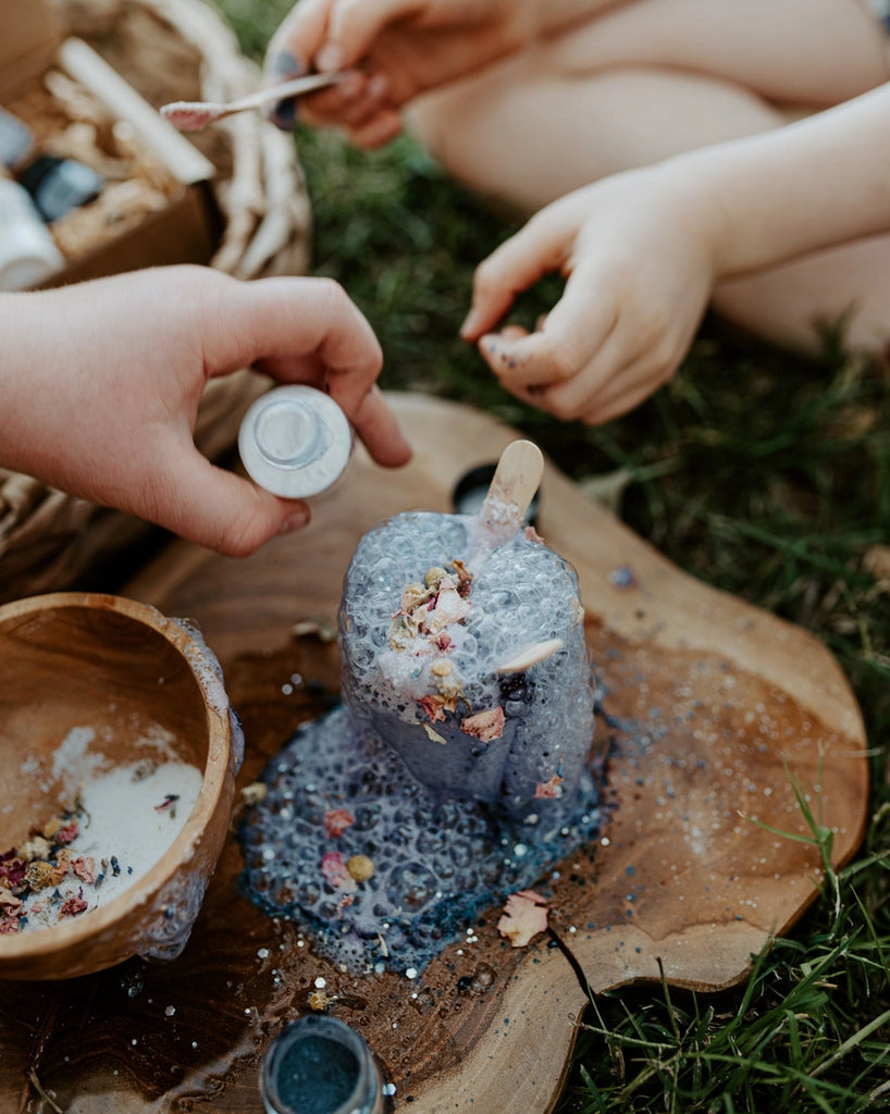 A small bottle of potion bubbles away on a wooden plate outside. Little Potion Co Colour Mood mini potion fit for happiness. Kit included one bottle of power essence, one bag of mood boost and one container of blue shift and one recipe card in a cardboard box. Made in Austrailia